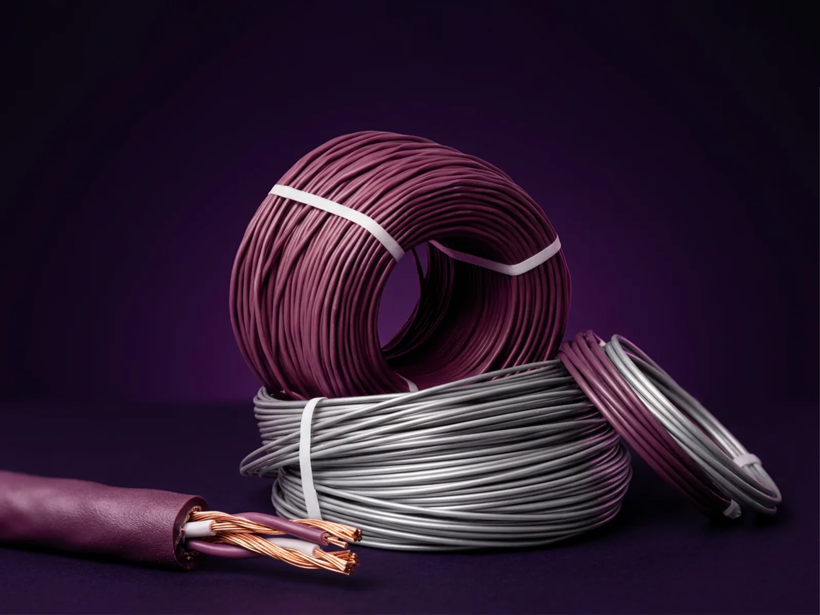 Coils of purple and silver twisted-pair cable on a deep purple surface, with one cut end showing the copper conductors inside.